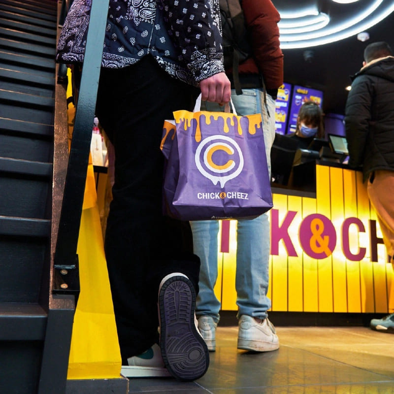 Customer holding a branded takeaway bag from Chick & Cheez while standing in line at the restaurant counter.